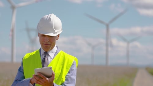 Engineer Using Tablet at Windmill Farm on Sunny Day