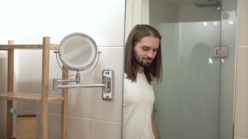 Mann im Badezimmer schaut in den Spiegel und berührt Gesicht