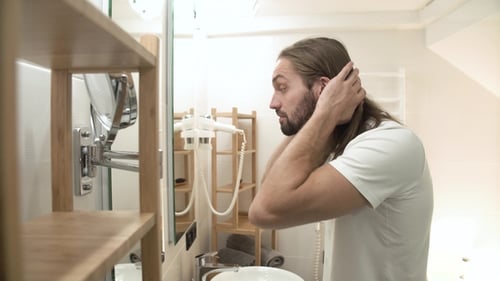 Mann im Badezimmer schaut in den Spiegel und berührt Gesicht