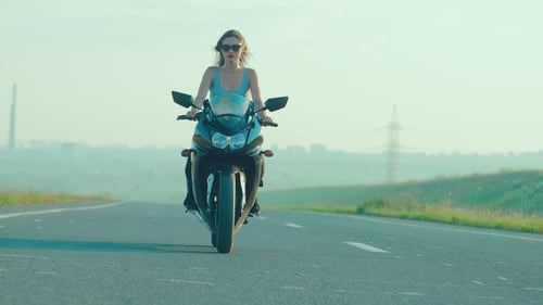 Sexy Woman Riding a Motorcycle During the Sunset Outside the City on the Road
