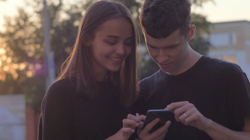 Couple Sharing Media in a Smart Phone in a Park with Buildings in the Background