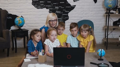 Happy Teacher Using Laptop with Pupils in the Classroom of Geography