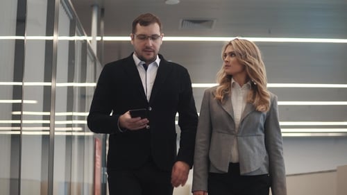 a Man and a Woman Walk Along the Foyer of the Business Center and Talk on the Move