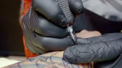 Ansicht von Hands of Tattoo Master Malen eines Bildes auf die Haut des Kunden, mit einer elektrischen Tattoomaschine
