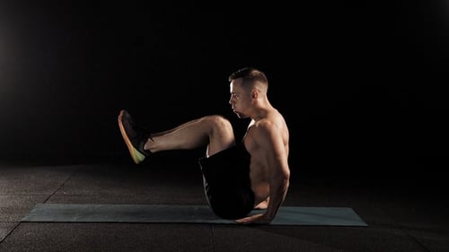 Young Strong Man Is Training in a Fitness Center, Lying on Sports Mat