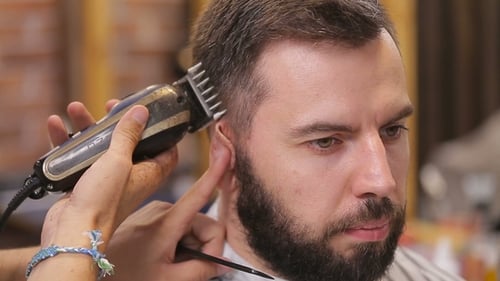 Meister schneidet Haare und Bart von Männern im Barbershop, Friseur macht Frisur für einen jungen Mann