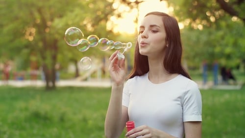 Young Woman Blowing Bubbles in Sunny Park
