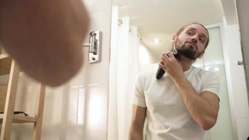 Man Shaving Face With Trimmer Looking In Mirror