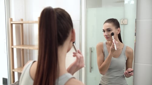 Young Woman Applying Makeup in Bathroom Mirror