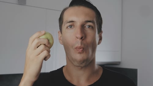 Young Man Eating Green Apple at Home in the Kitchen