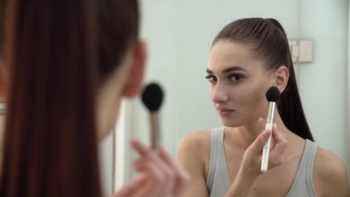 Face Makeup. Woman Using Powder And Looking In Mirror