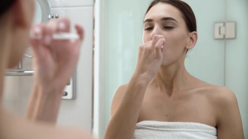 Young Woman Brushing Teeth in Bathroom Mirror