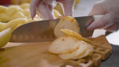 View of Hand of Cook, Wearing Plastic Gloves, Is Cutting Spiced Cheese on a Wooden Board in Kitchen