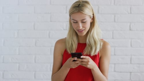 Woman Using Smartphone Against White Brick Wall