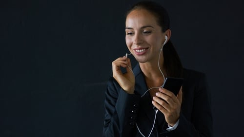 Woman in Suit Speaking Using Smartphone Earbuds
