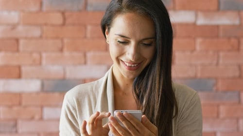 Woman Smiling While Using her Phone Indoors