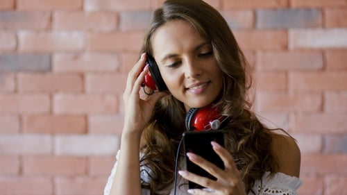 Woman Puts on Headphones and Looks at Phone