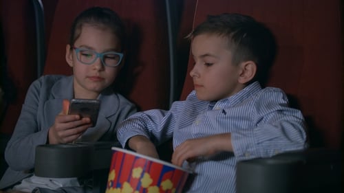 Children Eating Popcorn in Cinema. Kids Using Mobile Phone at Cinema