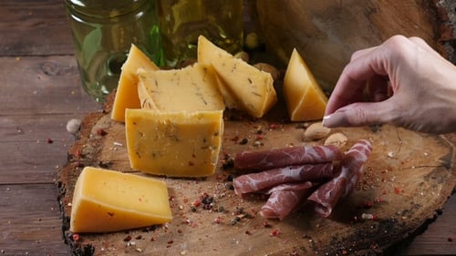 Variété de fromages sur fond en bois. Main féminine ajoute une tranche de prosciutto