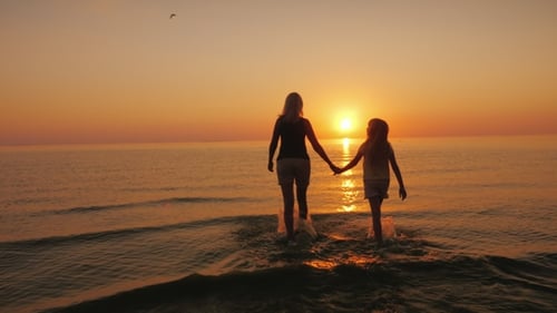Woman and Child Walking into Sea at Sunset