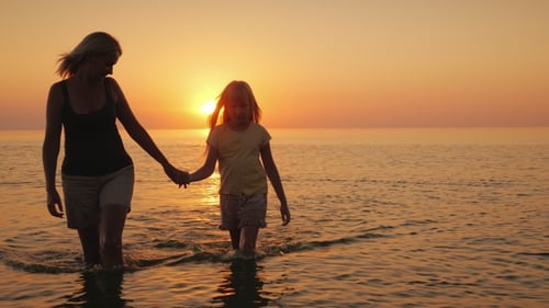 Woman and Child Walk on Beach at Sunset