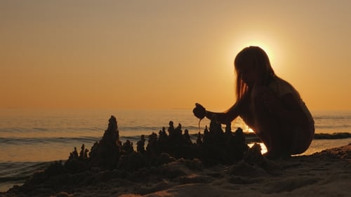 Silueta de un niño, construye un castillo de arena en la playa, una hermosa puesta de sol