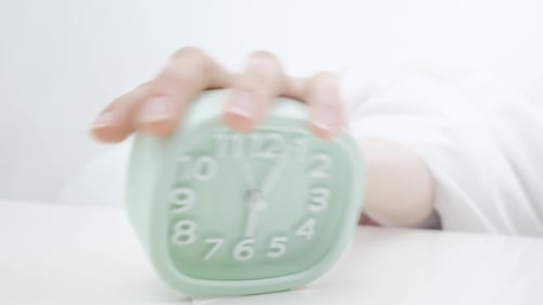 Aufwachen eines schlafenden Mädchens, das morgens den Wecker auf dem Bett stoppt.
