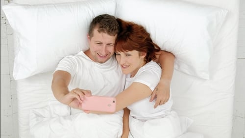 Blick von oben auf das junge attraktive Paar, das im Bett liegt und schöne Selfies auf dem Smartphone macht.