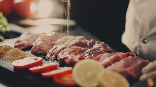 Chef Seasoning Raw Meat with Spices in Kitchen