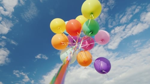 Colorful Balloons Floating Against Blue Cloudy Sky