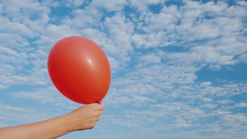 Hand Holds Red Balloon Against a Blue Sky