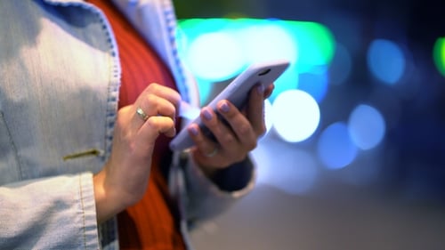 Hands of Young Woman Using Her Mobile Phone at Night Illuminated Street. Girl with Smartphone