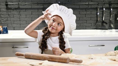 Little Cute Girl Pretending Chef in Cook Hat in Kitchen Rolling Dough with a Rolling Pin Making
