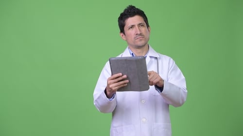 Hispanic Man Doctor Thinking While Using Digital Tablet