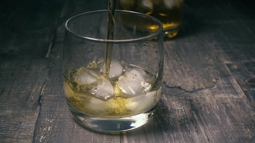 Alcoholic Beverage Pouring Into Glass with Ice Cubes