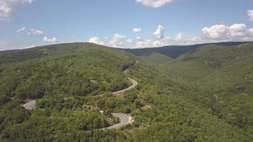 Aerial view of winding road with mowing cars and trucks in high mountain pass trough dense woods.