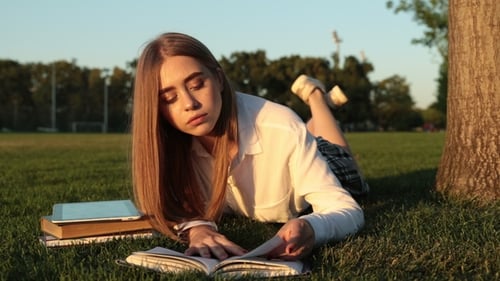 Woman Reads Book on Grassy Field in Sunlight