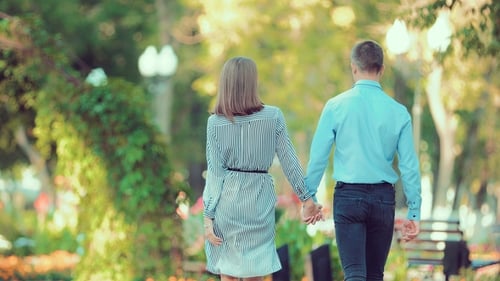 Young Couple Walk Through a City Park Together Heading Away From the Camera