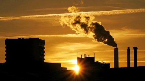 Silueta de planta de refinería con humo de chimenea contra puesta