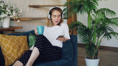 Woman Relaxes on Sofa with Phone and Drink