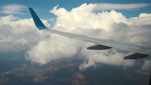 View of jet airplane wing from inside flying through white puffy clouds in blue sky.