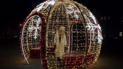 Woman Poses in Illuminated Christmas Ornament at Night