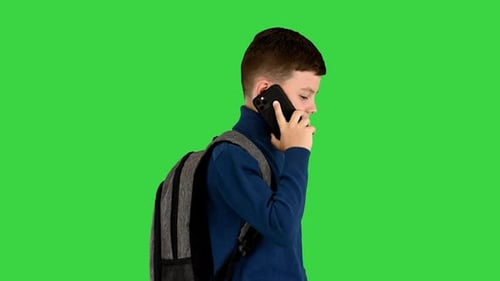 Schoolboy with a Backpack Talking on the Mobile Phone While Walking on a Green Screen Chroma Key