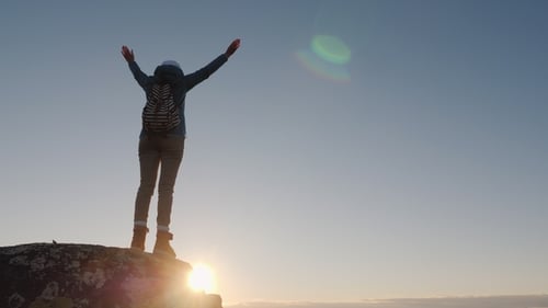 A Successful Woman Traveler at the Top of the Mountain Raises Her Hands Up