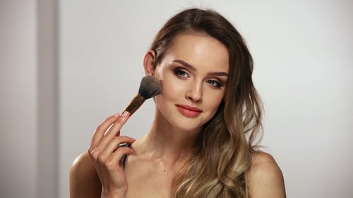Woman Applying Makeup With Brush in Studio