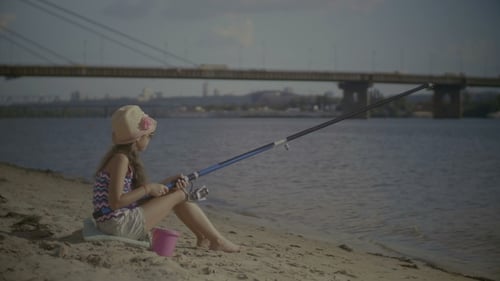 Porträt eines lächelnden Mädchens, das am Ufer sitzt und fischt
