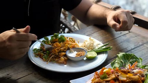 Man Eating Pad Thai at an Outdoor Cafe