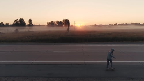 Girl Is Riding on a Skateboard Along an Empty Highway at Sunset