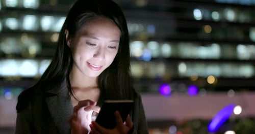 Une jeune femme d'affaires regarde un téléphone intelligent en ville la nuit