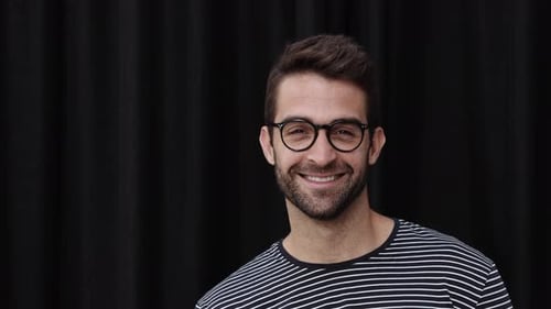 Smiling Man Puts on Round Glasses in Studio